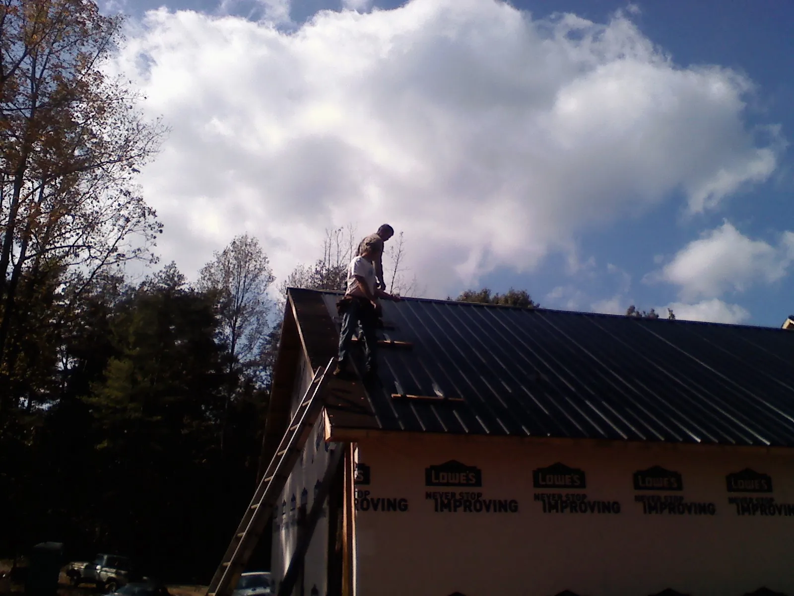 Roofer fastening dark metal panels high against a cloudy sky, from a Roof Inspection job in Millersburg